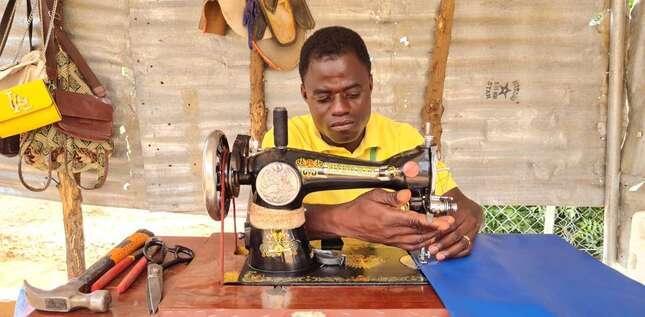 Un homme coud un tissu bleu avec une machine à coudre manuelle.