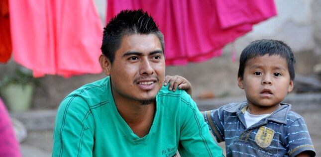 ChatGPT a dit :  Un homme souriant en chemise verte est assis à côté d’un jeune garçon qui pose sa main sur son épaule.