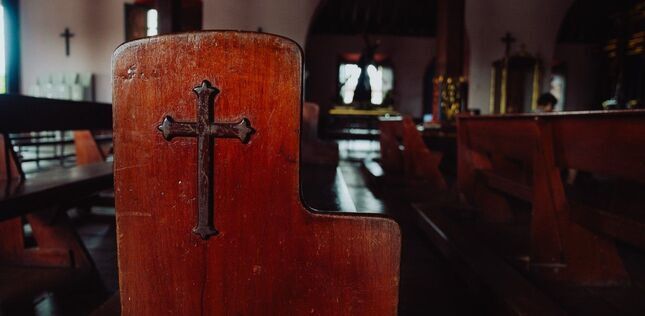 Banc d’église en bois avec une croix gravée, dans une lumière paisible.
