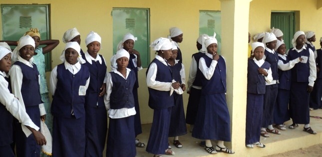 Groupe de jeunes filles en uniforme bleu marine et blanc, debout devant un bâtiment scolaire jaune.