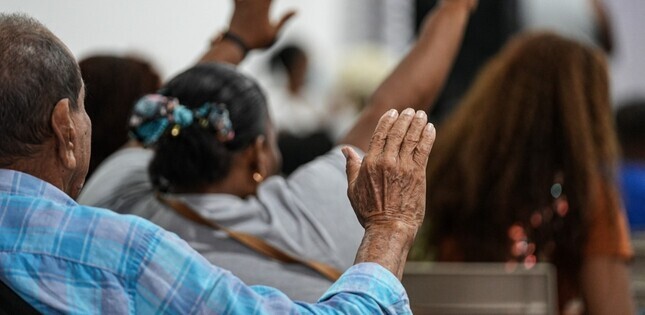 Personnes assises levant les mains en prière ou en louange, dans un lieu de culte.
