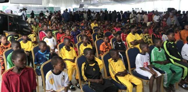 De nombreux enfants sont assis en rangées sur des chaises, rassemblés dans une grande salle lors d’un événement collectif.