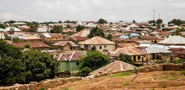 Vue d’ensemble d’une ville avec de nombreuses maisons aux toits en tôle, entourées de quelques arbres, sous un ciel couvert.