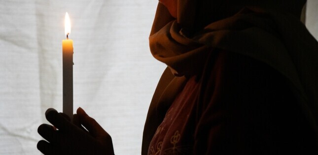 Une personne tient une bougie allumée devant elle, dans une ambiance sombre et recueillie.