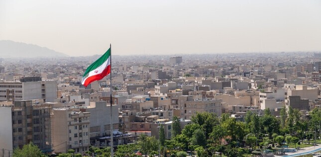 Vue panoramique d’une grande ville avec un drapeau iranien flottant au premier plan, au-dessus des immeubles.