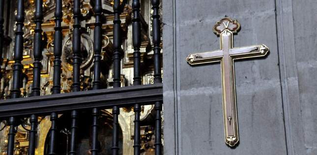 Une croix chrétienne est fixée sur un mur en pierre, à l’intérieur d’un bâtiment religieux.