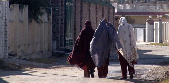 Trois femmes marchent ensemble dans une rue résidentielle, vêtues de longs voiles couvrant leurs épaules.