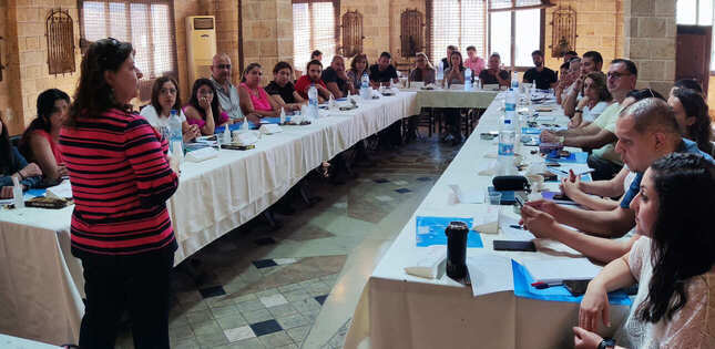 Une femme s’adresse à un groupe de personnes assises autour de tables disposées en U lors d’une session de formation.