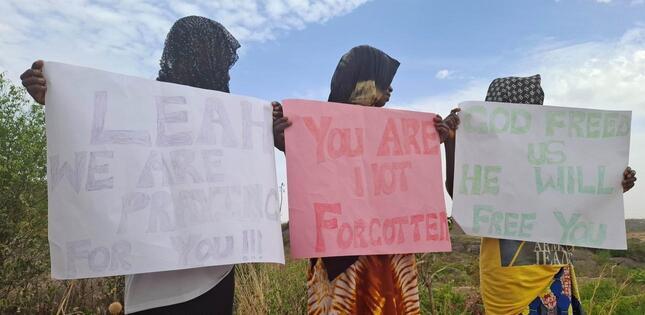Trois femmes tiennent des pancartes à l’extérieur, écrites en anglais.