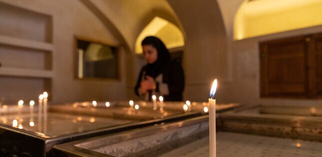 Bougies allumées au premier plan, avec une femme en prière floue à l’arrière-plan dans un intérieur voûté.