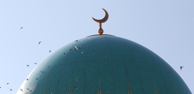 Dôme d’une mosquée, surmonté par le croissant islamique, avec des oiseaux volant autour.