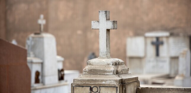 Tombe surmontée d’une croix en pierre blanche dans un cimetière.