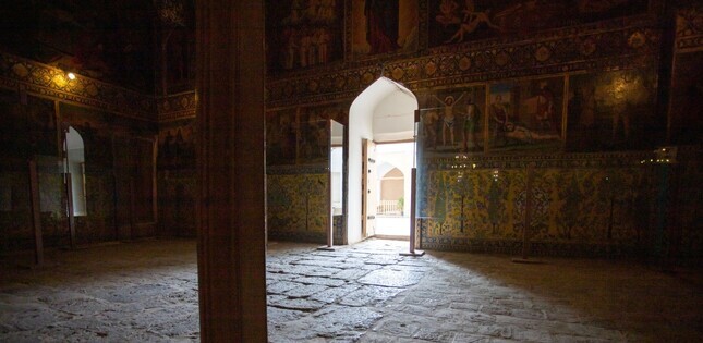 Vue sombre de l’intérieur d’une église. La pièce donne sur une porte baignée de lumière.