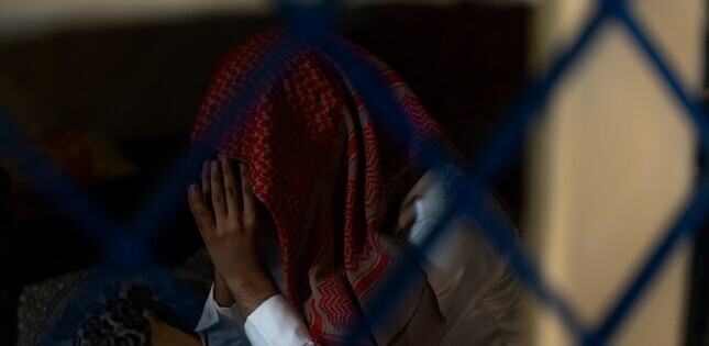 Vue d’une personne en prière, le visage dissimulé derrière ses mains et un foulard.