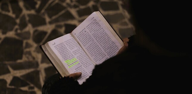 Vue de dos d’une personne lisant une bible en arabe, avec plusieurs passages surlignés.