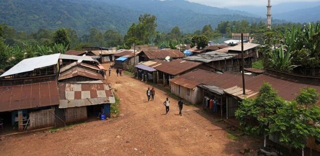 Vue d’une petite ville d’Éthiopie, avec ses habitations aux toits de tôle bordant une route en terre, au pied de collines verdoyantes.