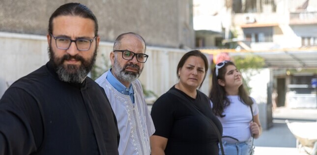 Vue de trois adultes (deux hommes, dont un en tenue religieuse, et une femme) et une adolescente à l’extérieur d’un bâtiment.