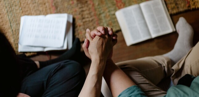 Vue de deux chrétiens se tenant les mains pendant un temps de prière, avec des bibles ouvertes à leurs côtés.