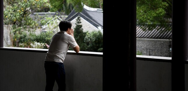 Vue d’un homme observant l’extérieur depuis une galerie, dans un moment de réflexion et de recueillement.