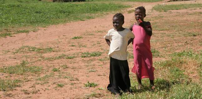 Vue de deux jeunes enfants sur un chemin de terre bordé de végétation.