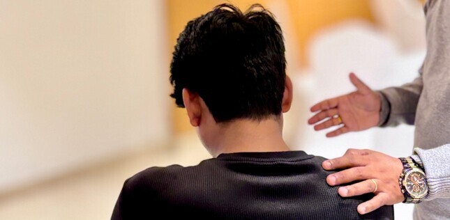 Vue d'une personne posant une main sur l'épaule d'un jeune homme pendant un temps de prière.