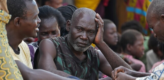 Vue d'un homme assis au milieu de plusieurs personnes, la main posée sur la tête.