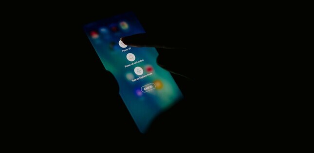 Vue d'un téléphone tenu dans l'obscurité, avec un doigt sur l'écran.